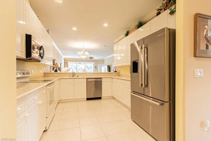 Kitchen with stainless steel appliances, a chandelier, light tile patterned floors, white cabinets, and recessed lighting