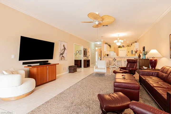 Living room with light tile patterned floors, ornamental molding, a chandelier, and ceiling fan