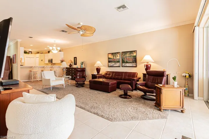 Living room featuring crown molding, light tile patterned flooring, a ceiling fan, and a chandelier