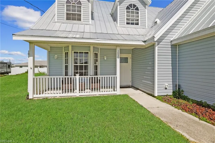Doorway to property featuring a porch, a yard, and a metal roof