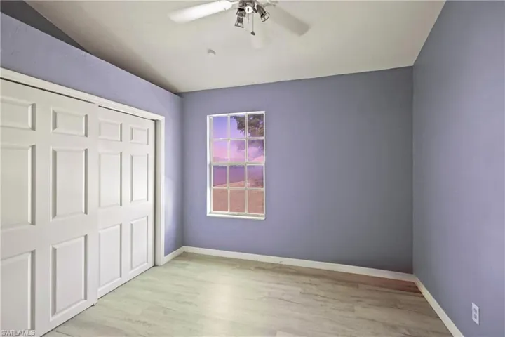 Unfurnished bedroom with wood finished floors, lofted ceiling, a closet, and ceiling fan