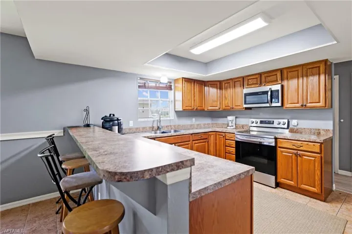 Kitchen featuring a peninsula, appliances with stainless steel finishes, a kitchen breakfast bar, a raised ceiling, and light tile patterned flooring