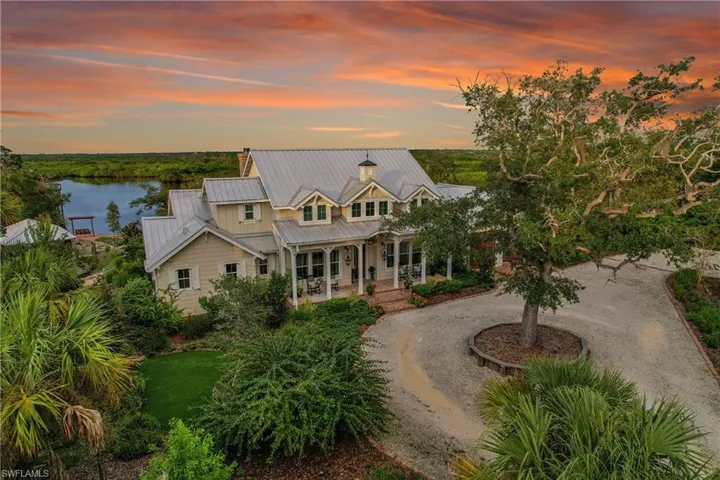 Front elevation showing the home's welcoming porch, circular drive, landscaping with mature oak trees, with preserve and water views beyond