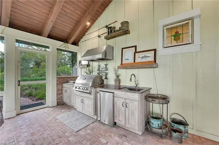 Covered, screened in outdoor living room equipped with built-in gas grill, cooler, beverage refrigerator and sink within custom cabinetry
