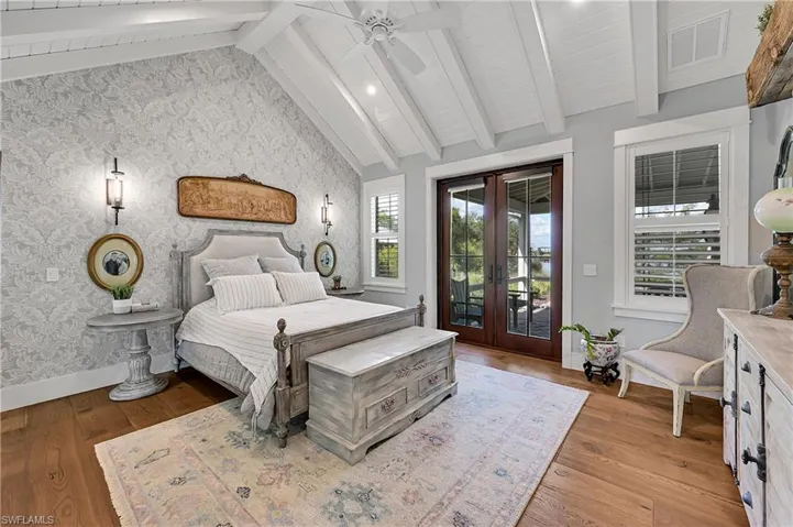 Serene primary bedroom featuring vaulted, beam-accented ceilings, wide-plank hardwood floors and French doors opening to the screened patio with full size porch swing bed.