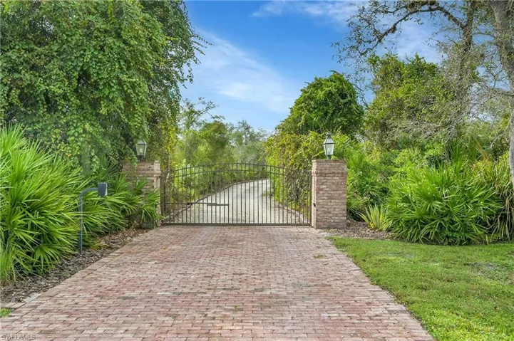 Private gated entrance featuring brick paver drive, brick columns topped with lanterns, and lush landscaping, offering a secluded and elegant approach to the property