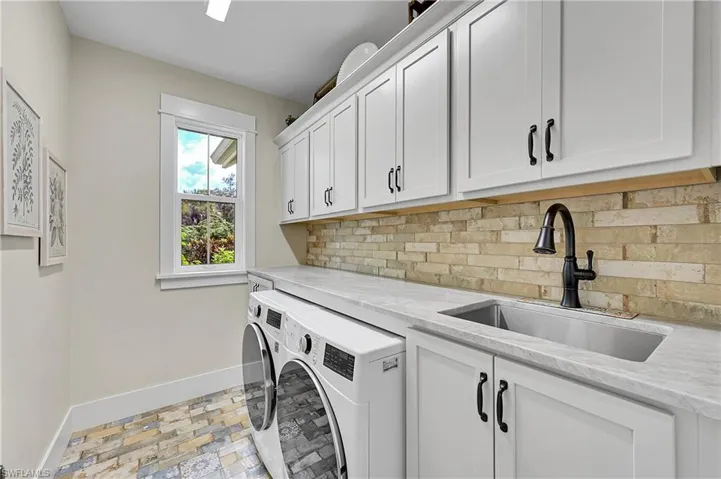 Well-appointed laundry room featuring custom cabinetry, stone countertops, utility sink and full-size washer and dryer