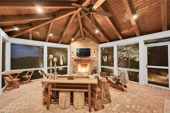 Elegant outdoor living room featuring a vaulted, beam-accented ceiling, gas-assisted brick fireplace, and expansive screened views.  Copper gas lanterns accent a space designed for year-round relaxation.