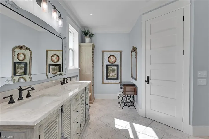 Double vanity with stone countertops, separate area for make-up table, decorative mirror, and abundant natural light