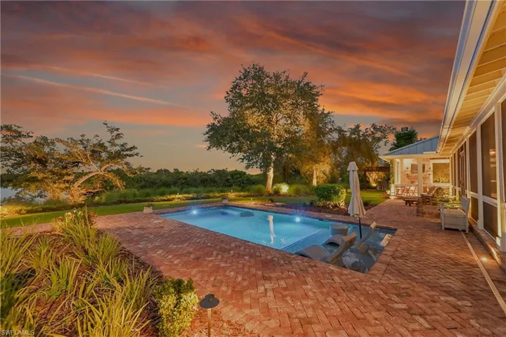 Illuminated pool overlooking the water, surrounded by brick pavers, creating a serene outdoor oasis