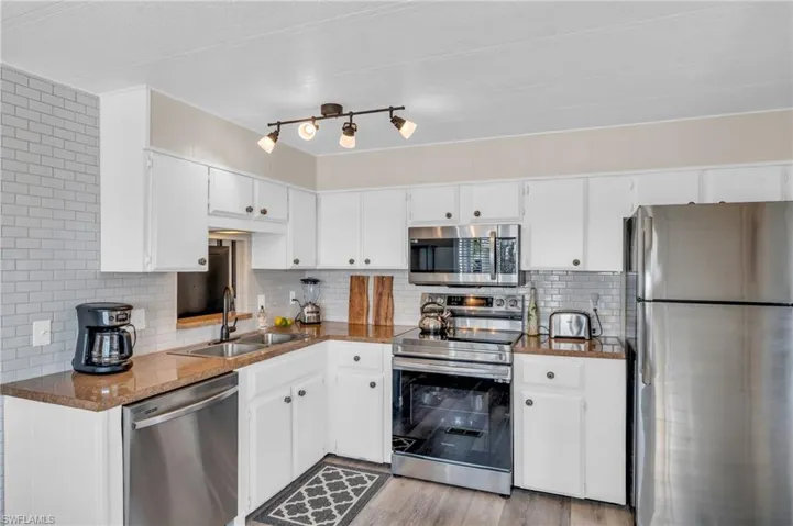 Kitchen featuring decorative backsplash, sink, white cabinetry, and stainless steel appliances