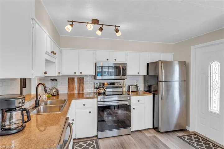 Kitchen with white cabinets, sink, LVP floors, tasteful backsplash, and stainless steel appliances