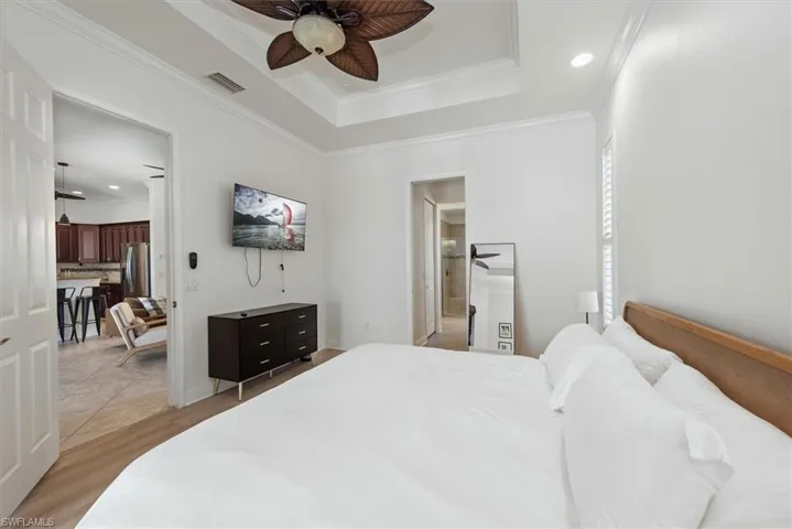 Bedroom featuring stainless steel fridge with ice dispenser, light wood-style flooring, crown molding, a raised ceiling, and recessed lighting