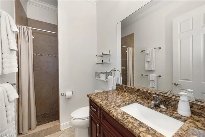 Full bathroom with crown molding, tiled shower, vanity, toilet, and tile patterned flooring