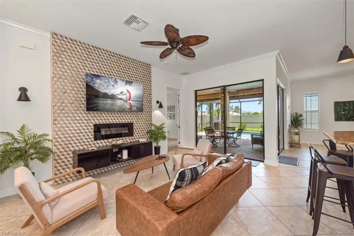 Living room featuring ceiling fan, crown molding, light tile patterned flooring, baseboards, and a fireplace