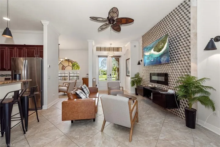 Living area featuring a ceiling fan, baseboards, an accent wall, crown molding, and ornate columns