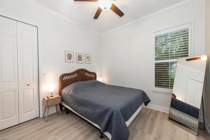 Bedroom featuring light wood-type flooring, ornamental molding, baseboards, a ceiling fan, and a closet