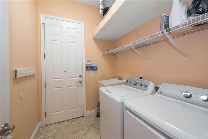 Laundry room featuring separate washer and dryer, light tile patterned floors, and baseboards