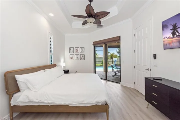 Bedroom featuring access to outside, a tray ceiling, light wood-style floors, ornamental molding, and baseboards