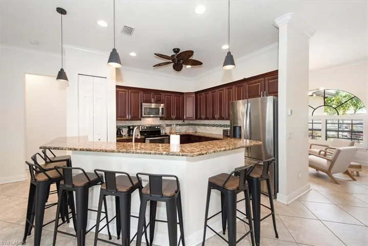 Kitchen featuring appliances with stainless steel finishes, a ceiling fan, crown molding, light tile patterned floors, and a kitchen bar