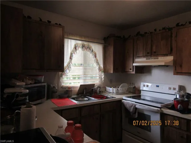 Kitchen with under cabinet range hood, white range with electric stovetop, light countertops, and stainless steel microwave