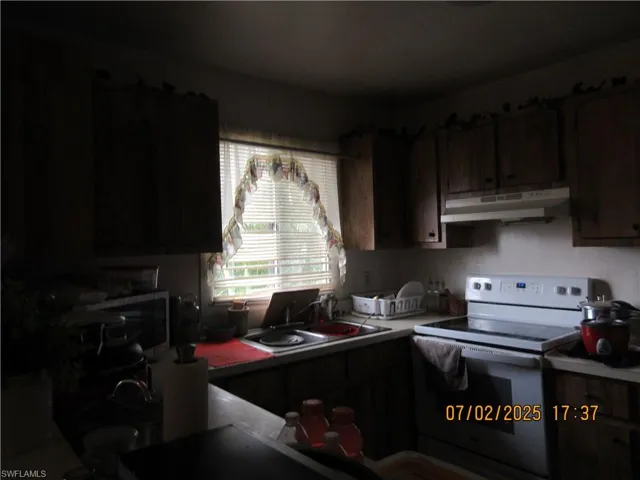 Kitchen featuring electric stove, under cabinet range hood, stainless steel microwave, and light countertops