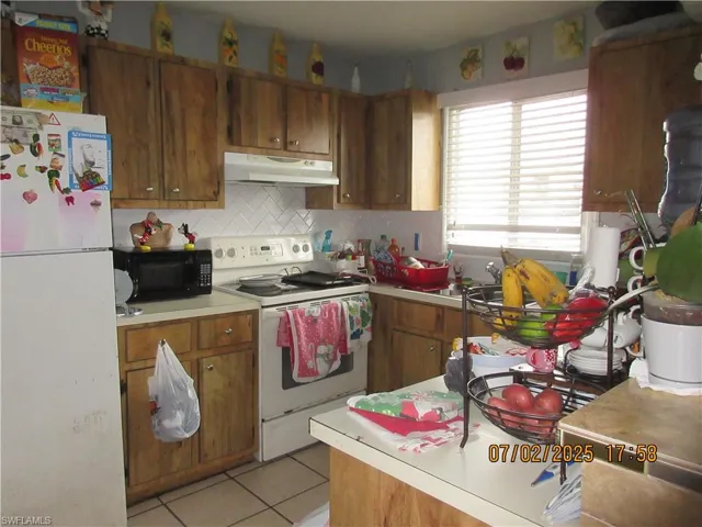 Kitchen with white appliances, under cabinet range hood, light countertops, and brown cabinetry