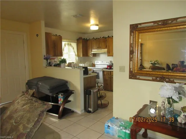 Kitchen featuring electric stove, under cabinet range hood, light tile patterned flooring, brown cabinets, and light countertops
