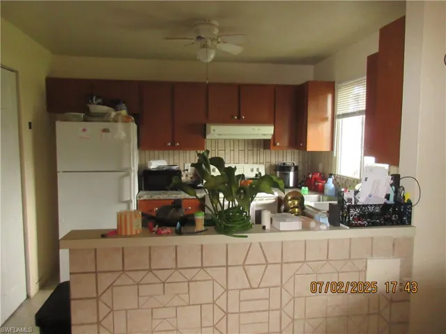 Kitchen featuring under cabinet range hood, a ceiling fan, brown cabinets, and light countertops