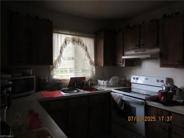 Kitchen featuring under cabinet range hood, white electric stove, stainless steel microwave, and light countertops