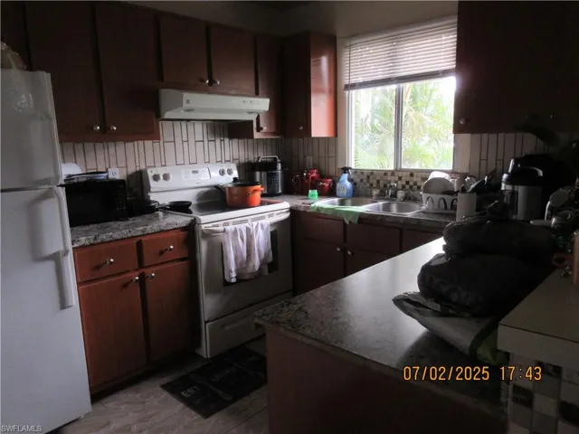 Kitchen featuring white appliances, ventilation hood, and backsplash