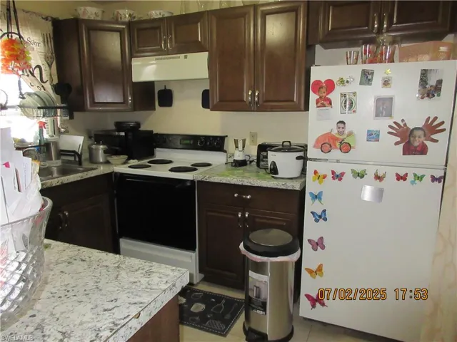 Kitchen with white appliances, under cabinet range hood, and light countertops