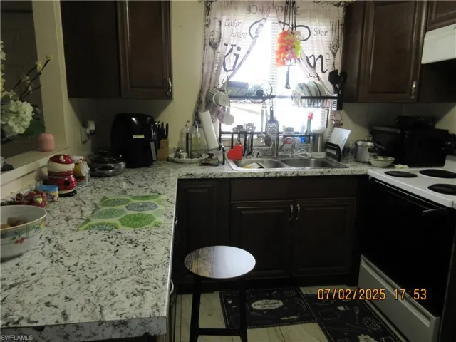 Kitchen with white electric stove, light countertops, extractor fan, dark brown cabinetry, and black microwave