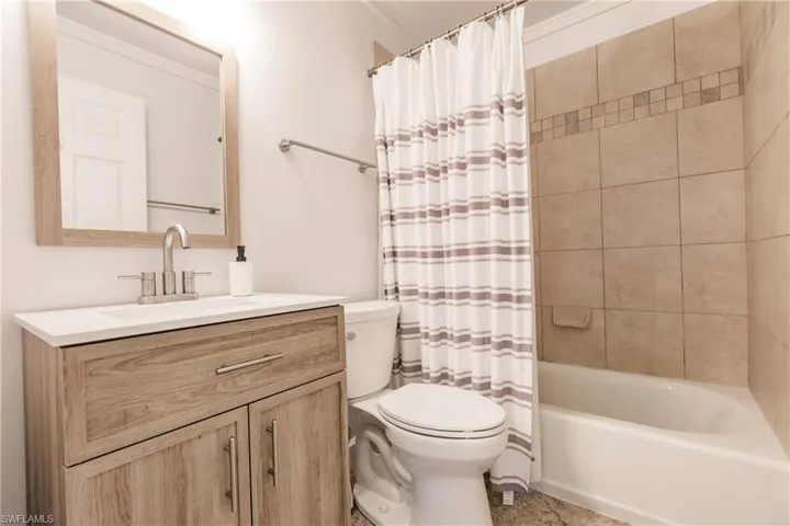 Full bathroom with vanity, shower / bath combination with curtain, crown molding, and toilet