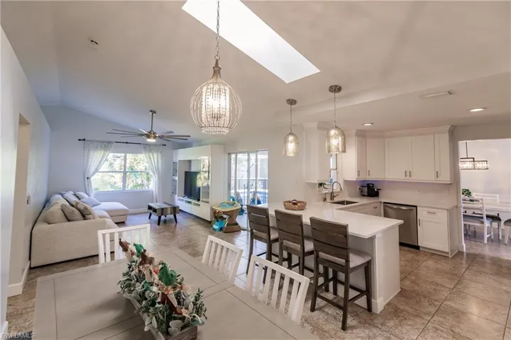 Kitchen featuring white cabinetry, sink, lofted ceiling with skylight, stainless steel dishwasher, and decorative light fixtures