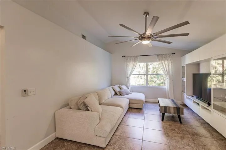 Living room with ceiling fan, tile patterned flooring, and lofted ceiling
