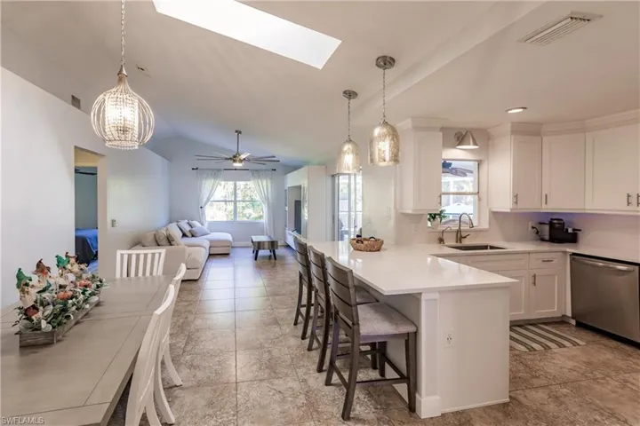 Kitchen featuring white cabinetry, a breakfast bar, hanging light fixtures, vaulted ceiling with skylight, and dishwasher