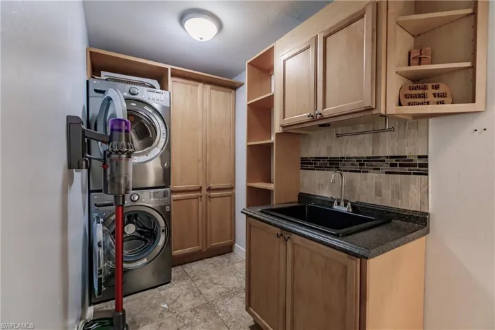 Laundry area featuring cabinets, stacked washer / drying machine, and sink
