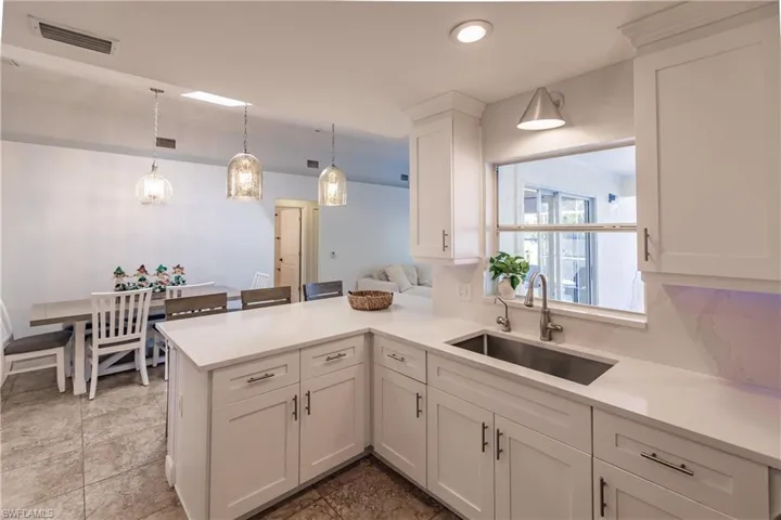 Kitchen featuring kitchen peninsula, white cabinetry, sink, and pendant lighting