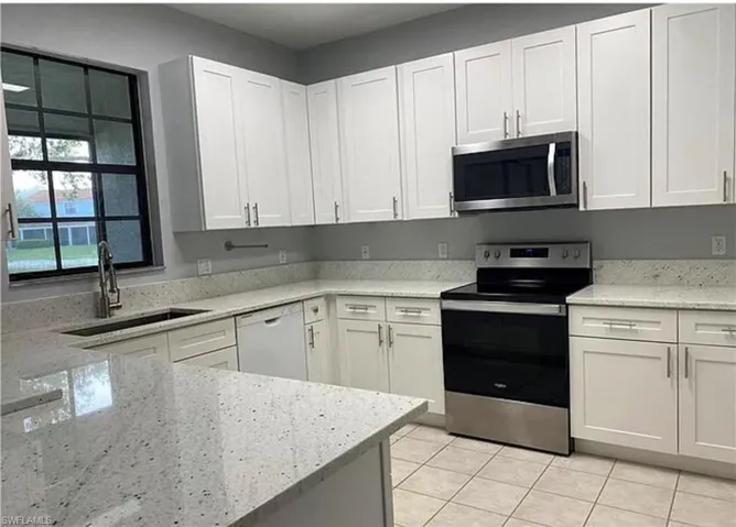 Kitchen with appliances with stainless steel finishes, light tile patterned flooring, white cabinetry, and light stone countertops