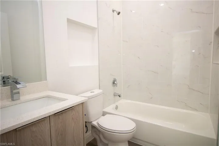 Full bathroom with vinyl-style flooring, toilet, vanity, and tiled shower / bath