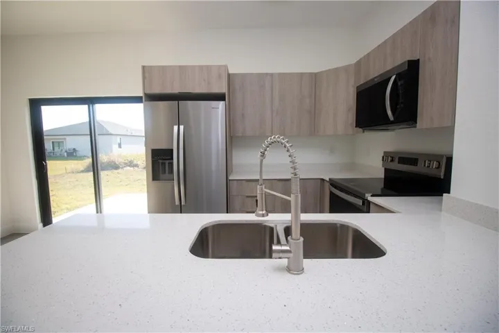 Kitchen featuring sink, light brown cabinets, appliances with stainless steel finishes, and hanging light fixtures