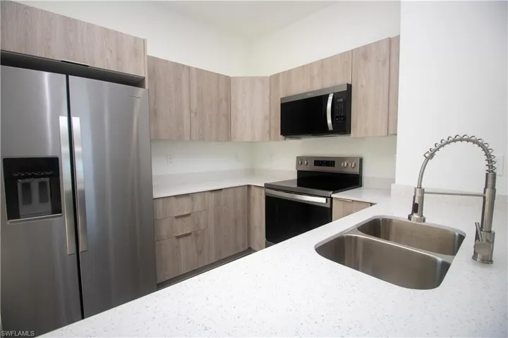 Kitchen featuring sink, light brown cabinets, appliances with stainless steel finishes, and hanging light fixtures
