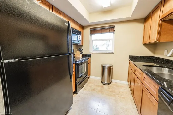 Kitchen featuring a raised ceiling, light tile patterned floors, sink, dark stone countertops, and black appliances