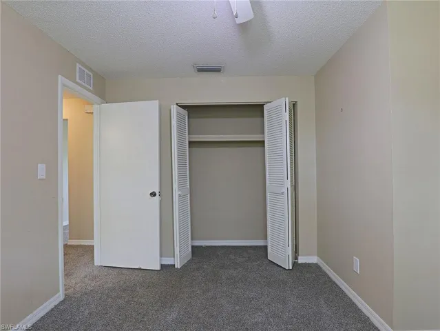 Unfurnished bedroom with ceiling fan, carpet, a textured ceiling, and a closet