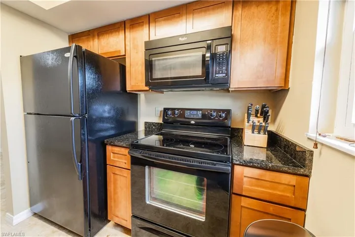 Kitchen featuring light tile patterned flooring, dark stone countertops, and black appliances