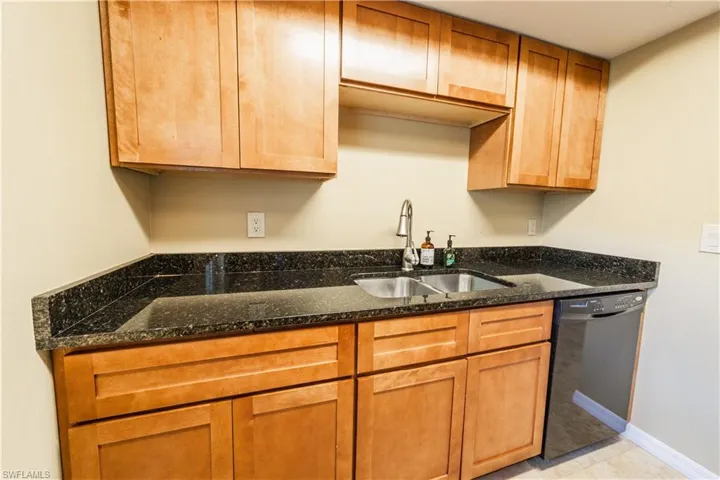 Kitchen with light tile patterned floors, black dishwasher, sink, and dark stone countertops