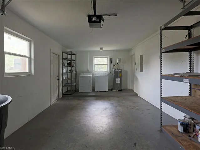 Garage featuring electric panel, a garage door opener, water heater, and separate washer and dryer