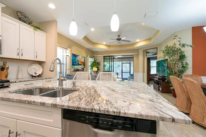 Kitchen featuring pendant lighting, dishwasher, light stone countertops, white cabinets, and a ceiling fan.