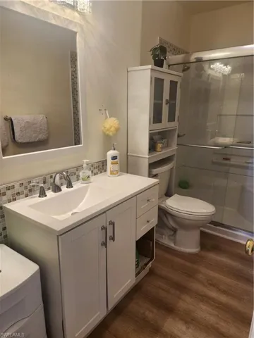 Full bath with toilet, wood finished floors, vanity, decorative backsplash, and a stall shower